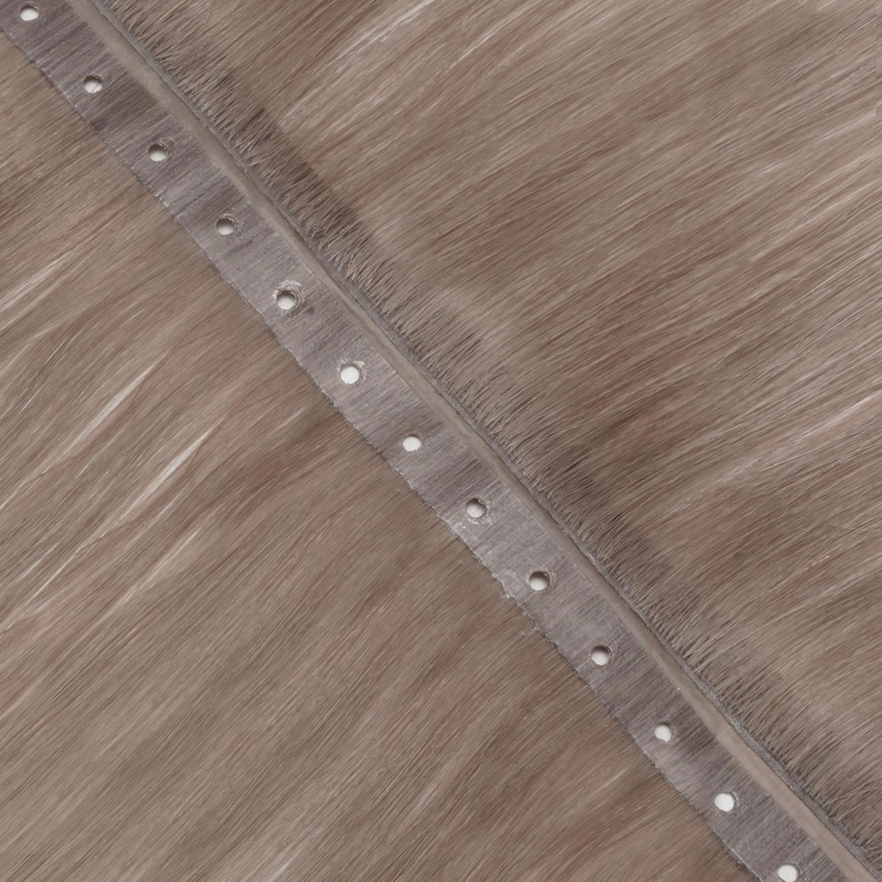 Close-up of a Flip Weft hair extension with a flat matte PU attachment area and bead holes positioned closer to one side for controlled installation.