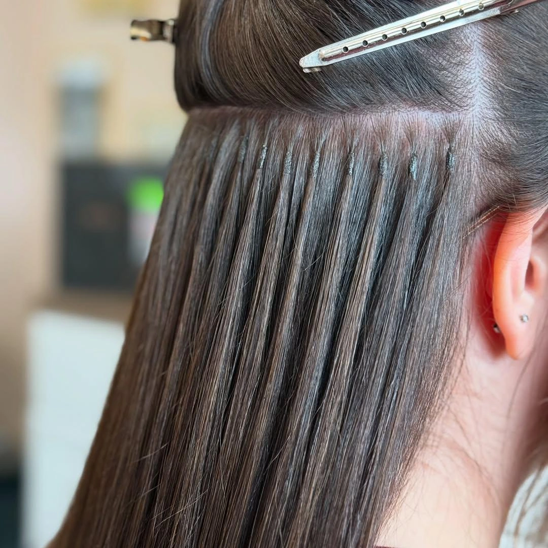 Keratin bond hair extension installation close-up showing strand-by-strand placement near the scalp